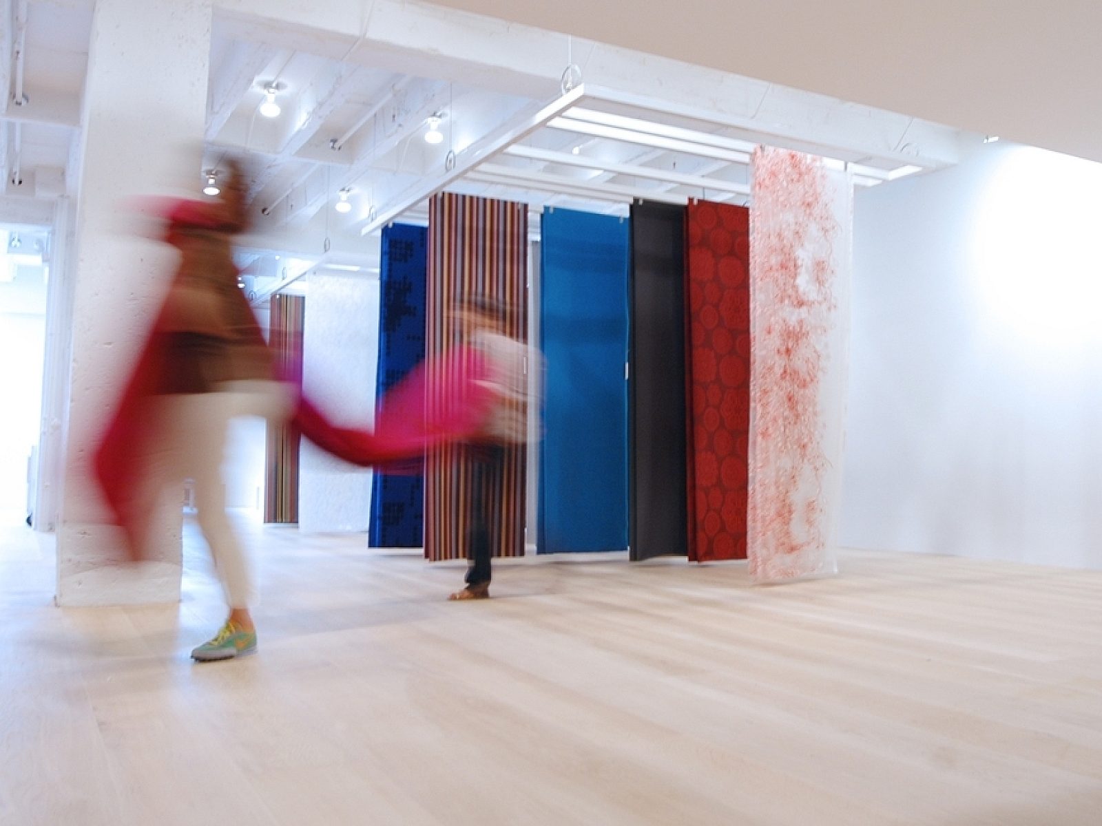 sheets of fabrics suspended from ceiling on light ash laminate floor with blurry images of people walking