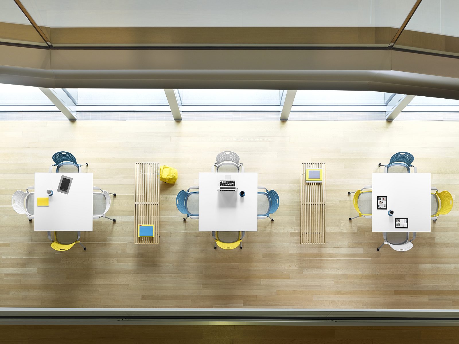 aerial view of white square tables with white, blue, and yellow seating on ash flooring