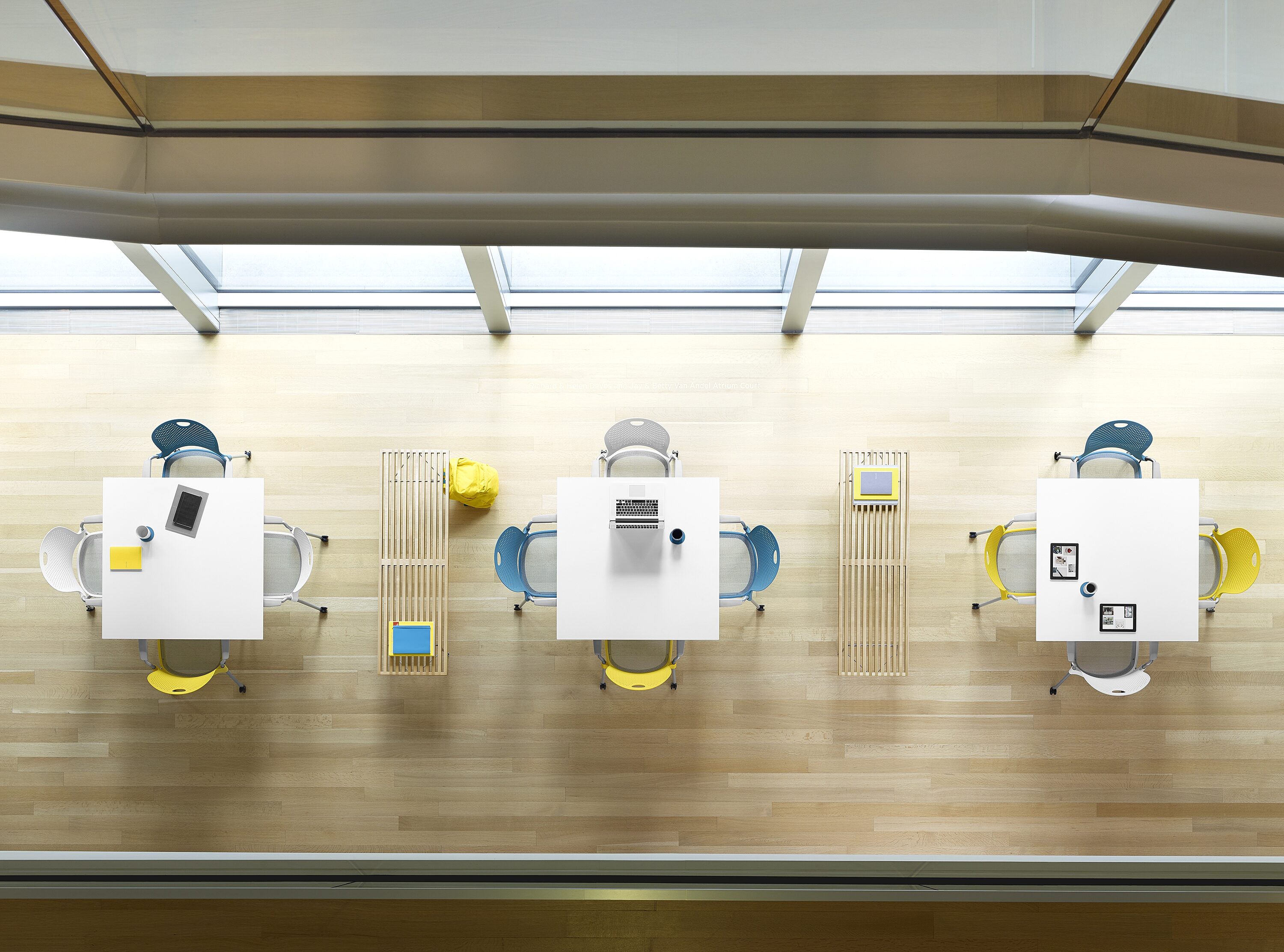 aerial view of white square tables with white, blue, and yellow seating on ash flooring
