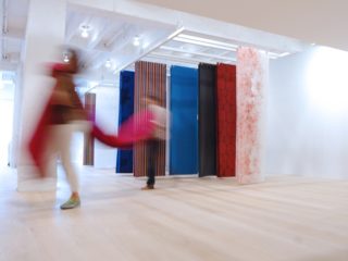 sheets of fabrics suspended from ceiling on light ash laminate floor with blurry images of people walking