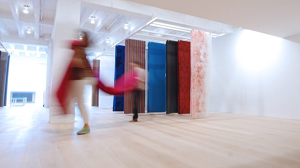 sheets of fabrics suspended from ceiling on light ash laminate floor with blurry images of people walking